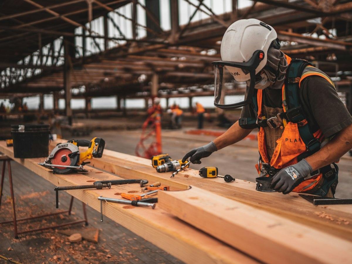 Carpenter in a hard hat and face shield cutting timber